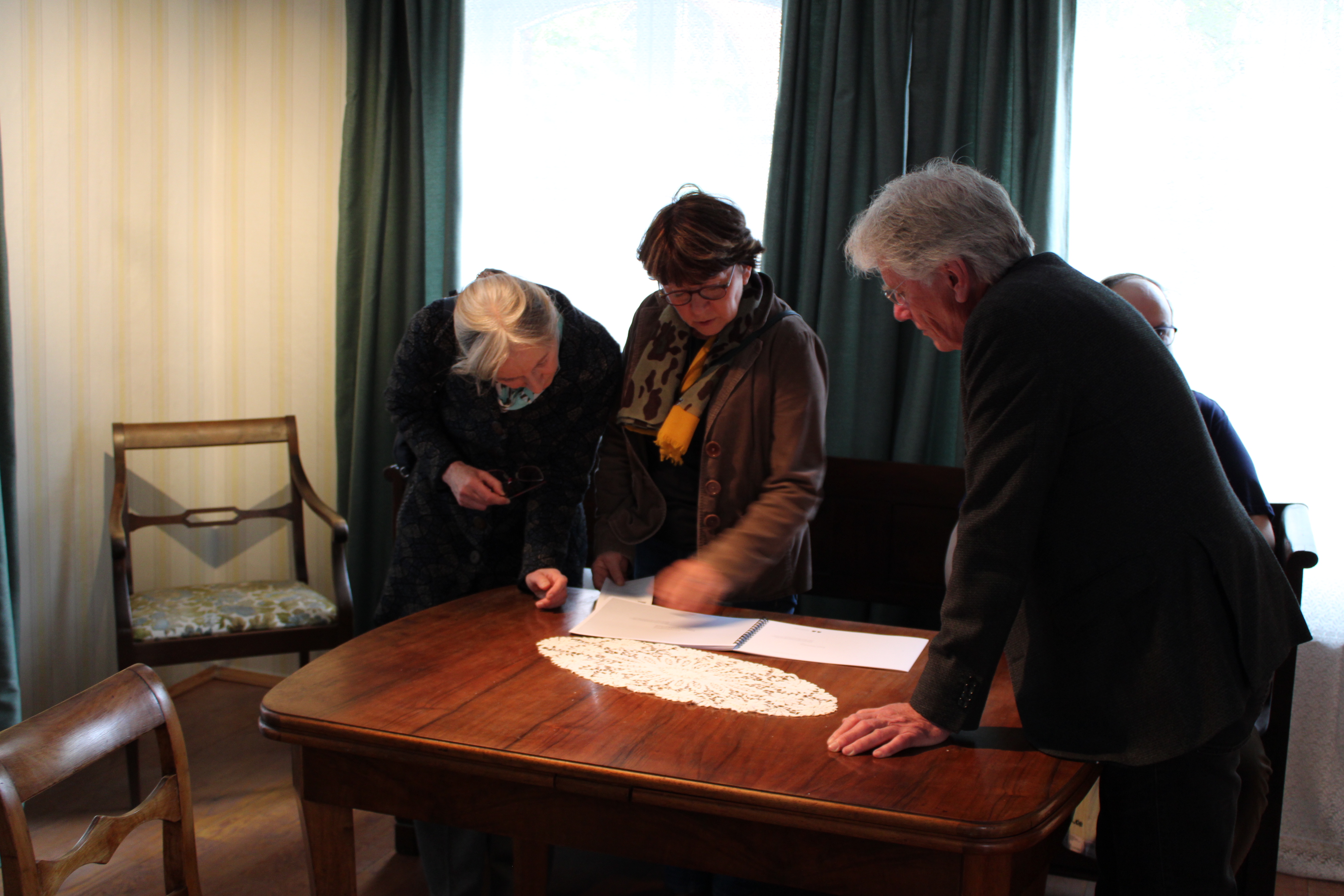 Drei Personen sind über einen historischen Tisch gebeugt und lesen ein Manuskript aus der Ausstellung.
